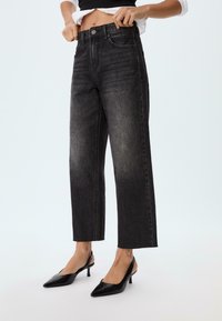 Jeans neri a vita alta con taglio dritto, texture sbiadita e orlo grezzo. Abbinati a décolleté nere a punta con slingback.