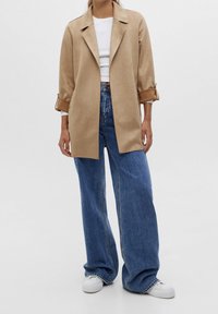 Beige faux-suede trenchcoat met oversized kraag, opgerolde boorden en een rechte snit, gecombineerd met hoge taille wijde blauwe denim jeans.