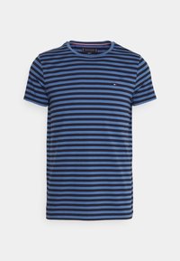 Pasiasta koszulka z poziomymi liniami w różnych odcieniach niebieskiego i granatowego. Okrągły dekolt, krótkie rękawy i akcent z logo na piersi.