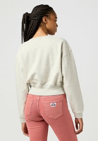 Felpa grigia chiara a maniche corte con scollo rotondo e polsini a costine, abbinata a jeans rosa a vita stretta con tasche posteriori cucite.