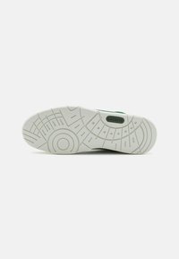 Fehér gumis sneaker talp, textúrált mintázattal, amely körkörös és lineáris motívumokat tartalmaz. Figyelemfelkeltő zöld márkázás "LACOSTE" részlettel.