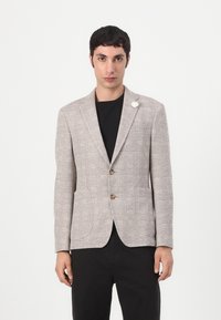 Hellbrauner, strukturierter Blazer mit Karomuster, einreihigem Design, zwei vorderen Taschen und braunen Knöpfen. Weißes Blumenpins-Detailed am Revers.