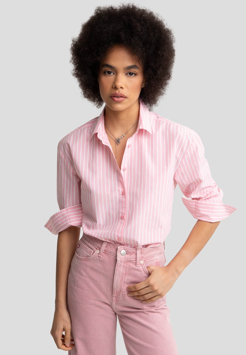 Camisa de botón a rayas rosa claro con mangas enrolladas, combinada con jeans rosa de cintura alta. Tejido suave, diseño casual, sin estampados.