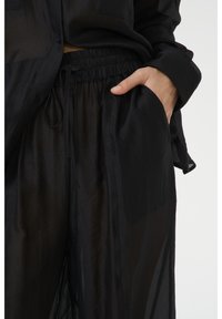 Ensemble en tissu noir transparent comprenant une chemise légère avec une poche et un pantalon à taille élastique, mettant en avant un design fluide et une texture douce.