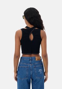 Zwart cropped tanktop met een keyhole rugontwerp en contrasterende stiksels, gecombineerd met high-waisted denim jeans met een label en achterzakken.
