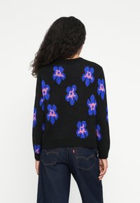 Zwarte trui met blauwe en roze bloemenpatronen, ronde hals, lange mouwen en structuurgebreide ontwerpelementen. Gestyleerd met donkere jeans.