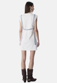 Vestido corto blanco con tirantes de denim, con un diseño sencillo y corte recto. La parte trasera presenta un acabado limpio y un detalle mínimo.