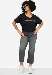 T-shirt noir court avec le texte "Cropped Flared", associé à un jean évasé gris et des baskets montantes blanches. Un design de tenue simple et décontracté.