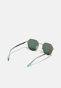 Ochelari de soare octogonali cu lentile verzi închise, cadru din metal aurit și vârfuri ale templelor cu gradient multicolor în nuanțe de teal și purpuriu. Pad-uri transparente pentru nas.