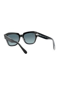 Gafas de sol de plástico negro con lentes de grado gris, diseño de marco angular y acentos transparentes en los bordes y las patillas.