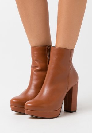 Brune læderankelstøvler med en glat tekstur, høj blokhæl og lynlåslukning bagpå. Med rundet tå og platformsål.