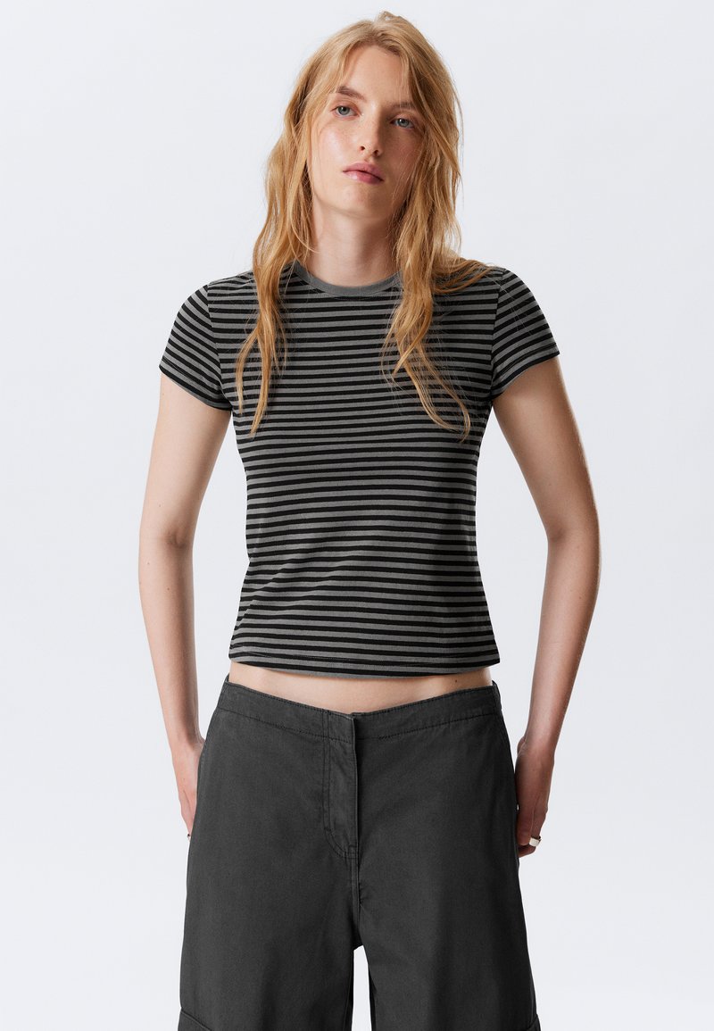T-shirt à rayures noires et grises à manches courtes avec un design ajusté et un col rond, accompagné de shorts gris foncé à coupe décontractée.