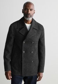 Paco de lana gris con mezcla, de diseño de doble botonadura, grandes solapas y dos bolsillos frontales. Tela texturizada notable y botones negros.