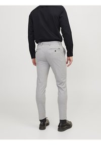 Dopasowane szare spodnie uszyte z miękkiego materiału, z dwiema kieszeniami i detalami w postaci guzików, w zestawie z czarną bluzką z długim rękawem i czarnymi butami.