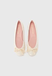 Ballerines beiges avec un revêtement texturé, doublure rose et un capuchon de orteil crème brillant ; dotées d'un nœud décoratif en corde de couleur claire.