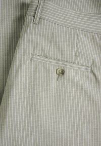 Tissu vert clair avec de fines rayures verticales blanches, montrant une poche arrière boutonnée et une ceinture de pantalon rayé.