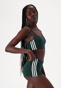 Conjunto de soutien desportivo e calções de algodão verde com riscas brancas na lateral, apresentando um design ajustado e alças ajustáveis. Textura suave.