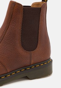 Braune Leder-Chelsea-Boots mit strukturiertem elastischen Seiteneinsatz, gelber Naht und Gummisohle, mit einer abgerundeten Fußspitze und niedrigem Absatz.