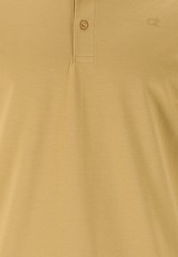 Gul pikétröja i texturerat tyg, med knappkrage och en liten logo på bröstet. Klassisk passform med korta ärmar.