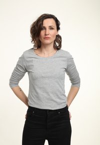 Graues Langarm-T-Shirt aus einem weichen Material mit rundem Halsausschnitt, getragen mit schwarzen Jeans. Einfaches Design, keine Muster oder Verzierungen.