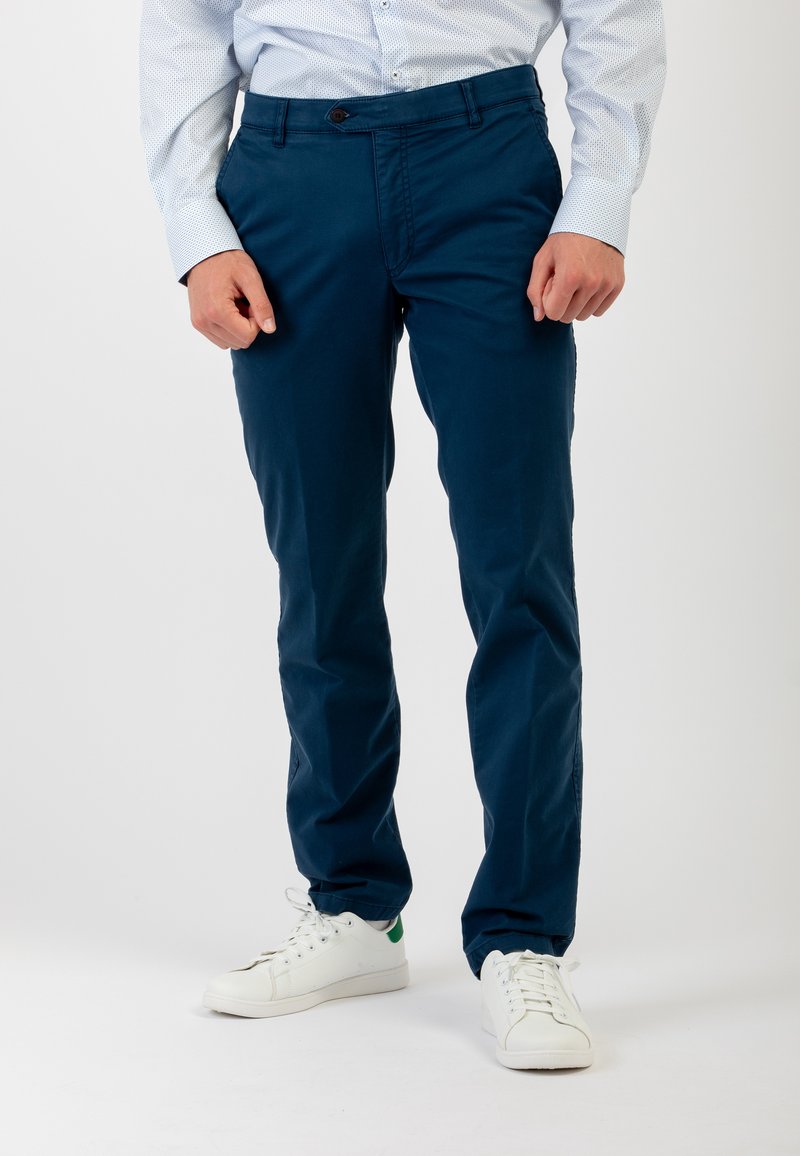 Pantaloni blu navy in cotone, con vestibilità dritta, tasche frontali e chiusura a un bottone, abbinati a sneakers bianche.