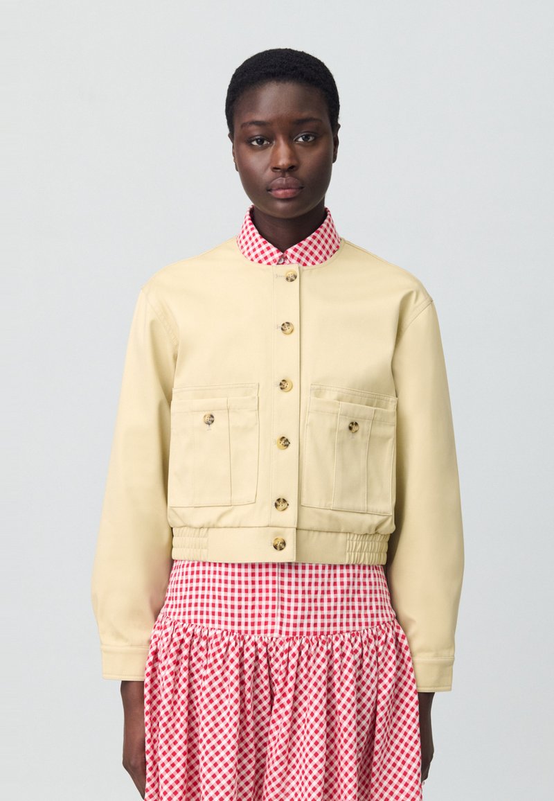 Veste beige raccourcie avec un col vichy rouge et blanc, dotée de deux poches avant, d'une fermeture à boutons et d'une taille élastique.