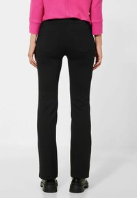 Svarta utsvängda byxor med en slät yta, som har två bakfickor och ett högt midjeband, ihop med en rosa ribbad långärmad topp.