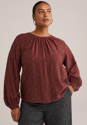 Blouse bordeaux avec encolure froncée et manches bouffantes. Motif texturé et coupe ample. Associée à un pantalon sombre à texture.