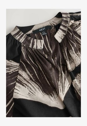 Bluza s črno-bež vzorcem, narejena iz lahkega materiala, z okroglim izrezom, nabranimi detajli in etiketo na ovratniku.