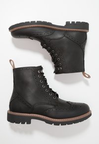 Stivaletti neri in pelle con lacci, dettagli brogue, punta rotonda, superficie testurizzata e suola in gomma con bordo marrone.