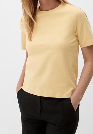 Gelbes T-Shirt mit kurzen Ärmeln aus weichem Stoff, mit einem runden Halsausschnitt und einer lockeren Passform, kombiniert mit schwarzen Hosen.