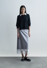 Mustast heegeldatud lühikeste varrukatega kampsun halli seelikuga, millel on valge pitsist ääris. Komplekti lõpetavad mustad rihmadega kingad.