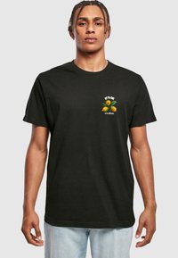 Black cotton t-shirt with short sleeves, featuring a graphic of lemons and text "IT'S OK to be different" on the chest in white and green.