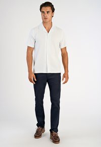 Koszula z krótkim rękawem w jasnoniebieski wzór, z kołnierzykiem i zapięciem na guziki, zestawiona z ciemnogranatowymi spodniami i brązowymi, casualowymi butami.