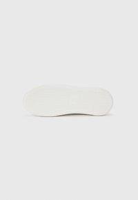 White sneaker sole with a textured pattern, featuring a smooth edge, central branding, and a clean design. Flat profile for stability.