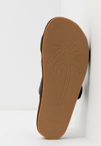 Black sandal with a textured upper, brown rubber sole featuring a palm tree motif and logo. Size 37 is displayed on the sole.