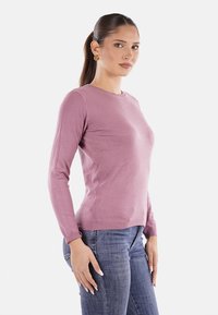 Maglione rosa chiaro a maniche lunghe con scollo rotondo, design aderente e texture liscia, abbinato a jeans di denim blu.