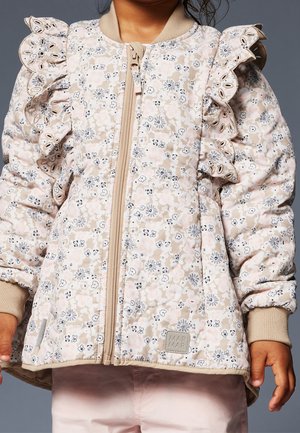 Bambino che indossa una giacca a piumino beige con stampa floreale, dettagli arricciati sulle spalle e chiusura frontale con cerniera, su uno sfondo semplice.