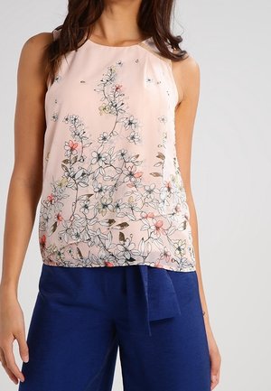Blusa sin mangas de color rosa claro con estampado floral multicolor, combinada con pantalones azul oscuro con detalle anudado en la cintura.