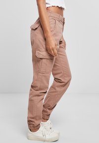 Kargo kalhoty v pudrově růžové bavlně s elastickými manžetami a bočními kapsami, s uvolněným střihem a hladkou texturou. Ozdobené kontrastním prošíváním.