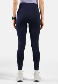 Hoch taillierte, marineblaue Leggings aus glattem, dehnbarem Material, mit einer Gesäßtasche und einer taillierten Passform, kombiniert mit weißen Sportschuhen.