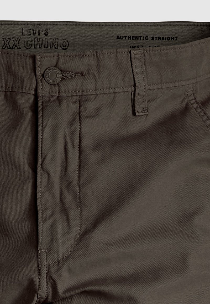 Pantalones chino de algodón marrón con corte recto, cierre de botón visible y detalle cosido en los bolsillos y la cinturilla.