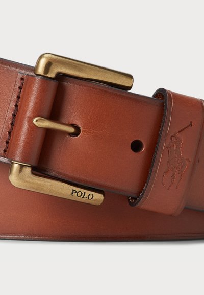 Läderbälte i tan med en mässingsspänne. Graverad "POLO" på spännet, med detaljerad sömnad längs kanterna och en dekorativ logotyp.