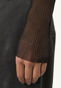 Schwarzes Netzoberteil mit langen Ärmeln, vertikaler Rippstruktur, transparenter Textur und tailliertem Schnitt. Eine Hand ist sichtbar und ruht auf einem dunklen Stoffhintergrund.