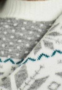 Weicher Strickstoff mit weißen, grauen und türkisfarbenen geometrischen und Zickzackmustern, gefaltet, um Textur und Designdetails zu zeigen.