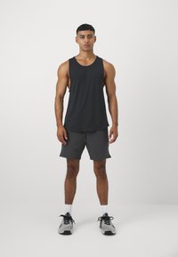 Fekete trikó, szürke rövidnadrág és szürke sportcipő. Az anyag sima, a rövidnadrág pedig laza szabású zsebekkel rendelkezik.