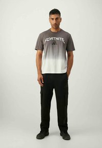Grå og hvit gradient T-skjorte med "FORTNITE" og Adidas-logo, sammen med svarte cargo-bukser og svarte sneakers.