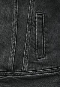 Κοντινή λήψη μαύρου τζιν υφάσματος με κάθετες και οριζόντιες ραφές και ορθογώνια σχισμή τσέπης.