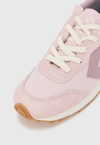 Lys rosa sneaker laget av semsket skinn og stoffmateriale, med rund tå, hvite snørebånd og en teksturert gummisåle med gummifarge.