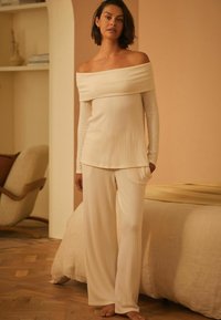 Off-shoulder, geribbelde pyjama set in crème, met lange mouwen en wide-leg broeken met zakken. Zachte textuur en Relaxte pasvorm.